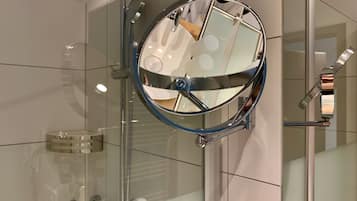 Une salle de bain moderne avec une douche à parois de verre, des robinetteries chromées et un miroir rond.