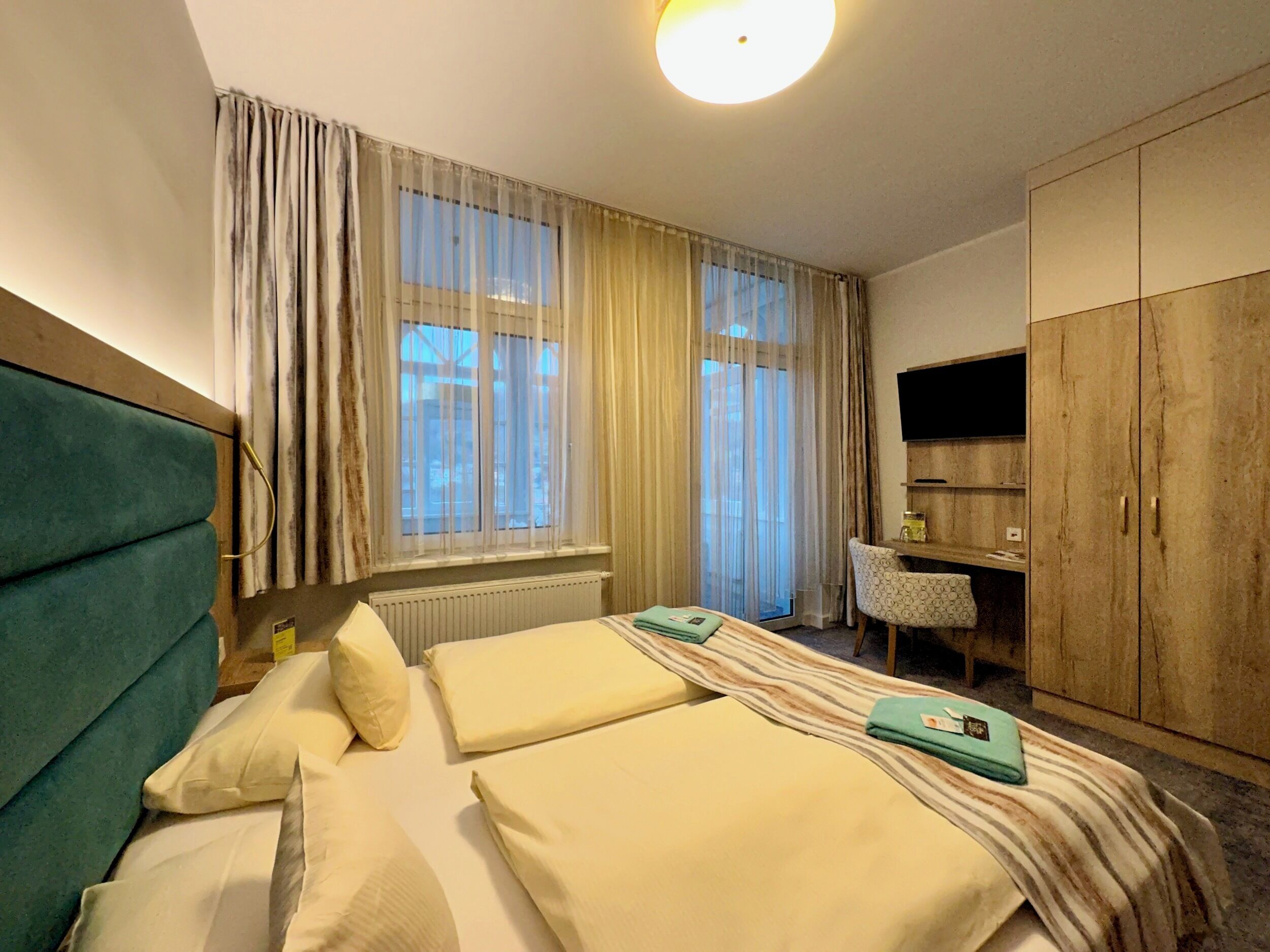 A hotel room with two beds, a desk, a chair, a television, and a wardrobe.