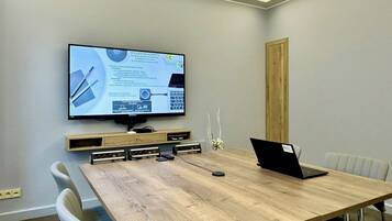 A conference room with a large flat-screen TV mounted on the wall, a wooden table, and several chairs.