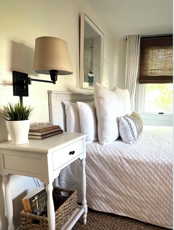 Cozy retreat with a comfortable bed, nightstand, and potted plant.