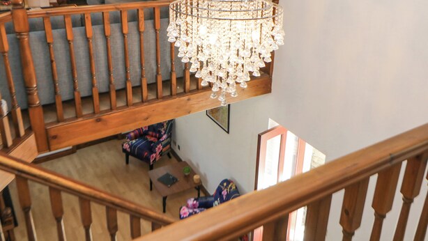 Um candelabro pendurado na balaustrada de uma escada de madeira, um sofá cinzento e uma estante em uma sala de estar.