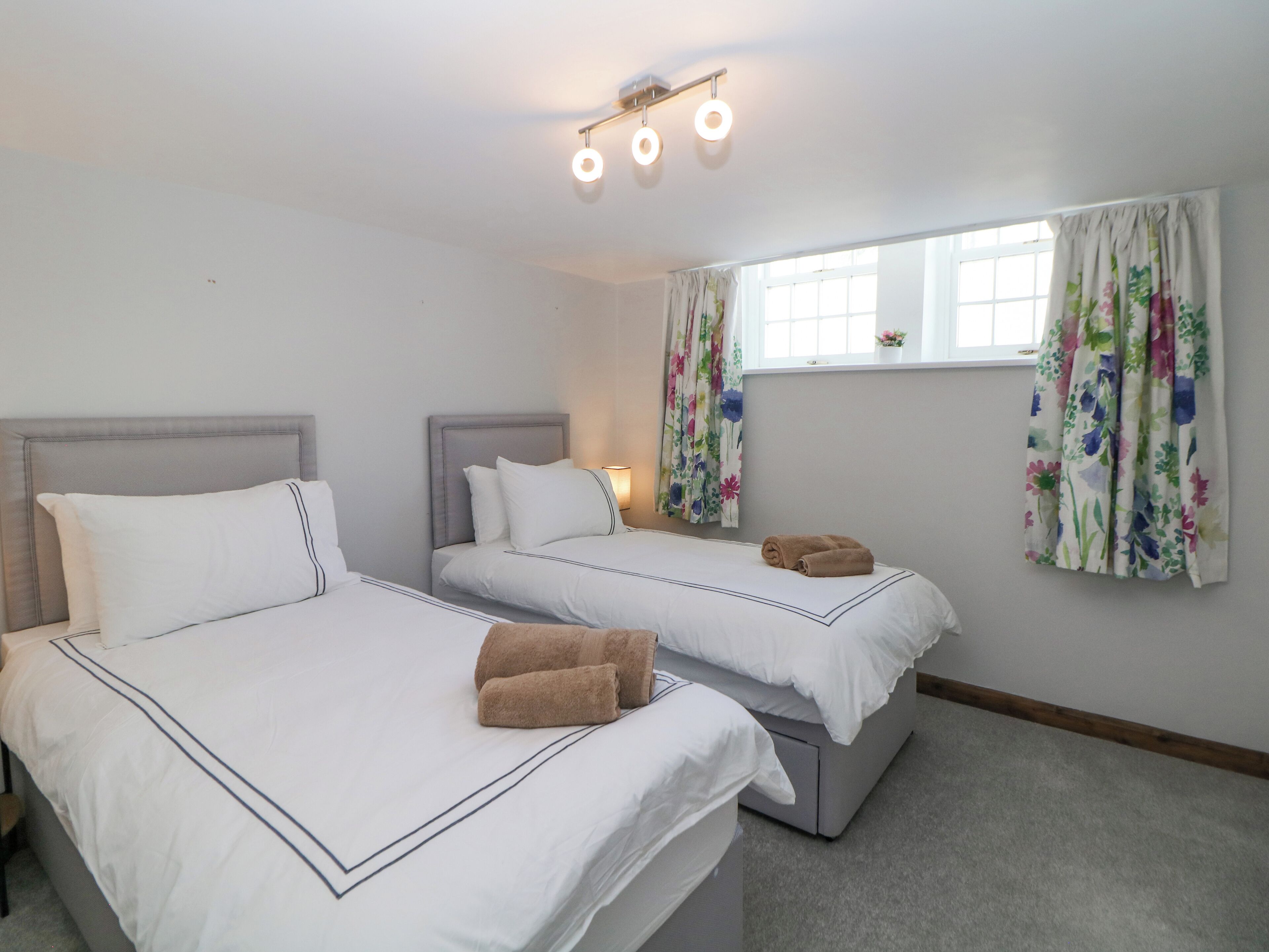 Habitación de hotel con dos camas, una ventana con cortinas florales y una lámpara en el techo.
