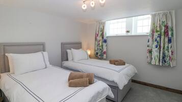 Habitación de hotel con dos camas, una ventana con cortinas florales y una lámpara en el techo.