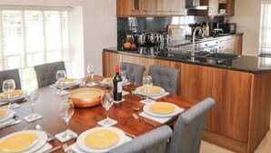 Cozinha moderna com armários de madeira, bancada preta e área de refeições com mesa para seis pessoas.