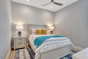 Un dormitorio con cama, mesitas de noche, lámparas y un ventilador de techo.