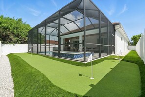 Una casa moderna con un patio acristalado, piscina y césped cuidado.