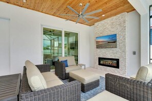 A modern outdoor living area with wicker furniture, a ceiling fan, and a fireplace. - Naples Coastal Retreat: Heated Pool, Hot Tub, (Naples)