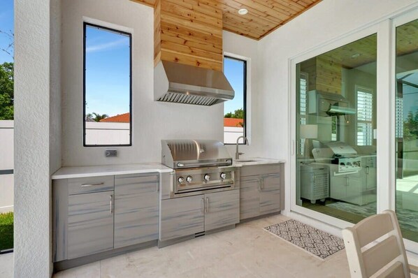 Una cocina exterior con estufa de acero inoxidable, campana extractora y una ventana.