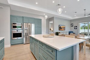 A modern kitchen with stainless steel appliances, teal cabinetry, and a large island.