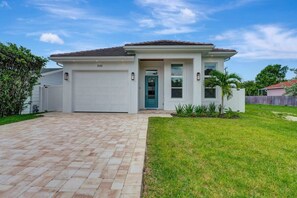 A single-story house with a garage, a front door, and a small front yard with grass and a palm tree. - Luxury Coastal Chic Retreat w/ Hot Tub & Pool (Naples)