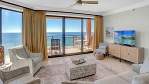 Ein geräumiges Wohnzimmer mit großem Fenster zum Meer, ausgestattet mit einer Couch, Sesseln und einem Fernseher.