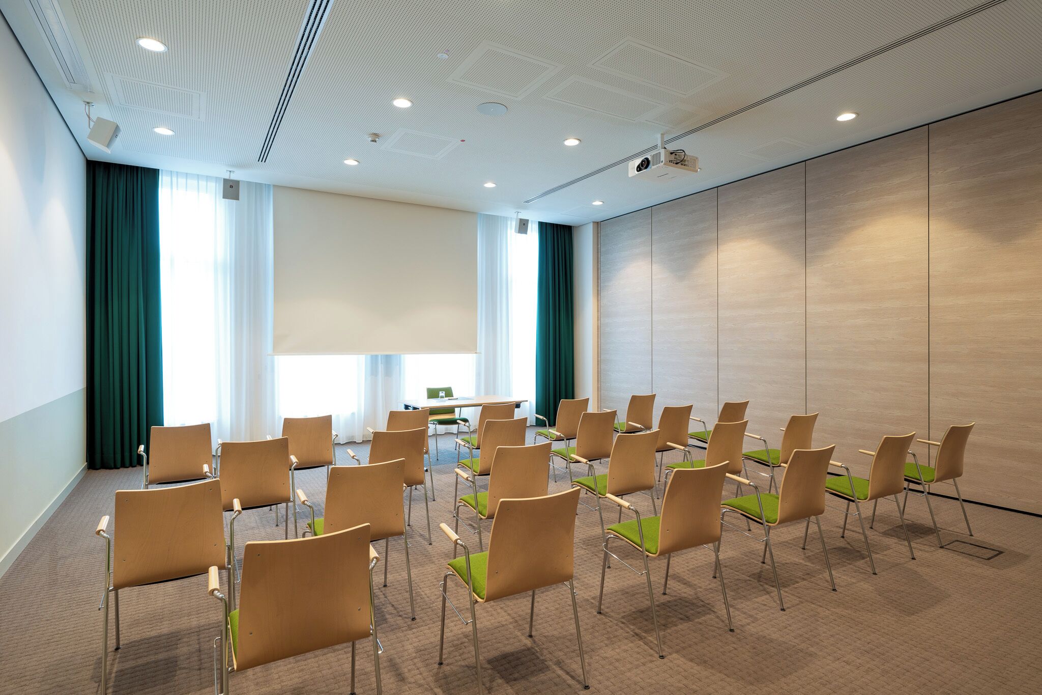 Un salón de conferencias con filas de sillas, un proyector y una pantalla grande.