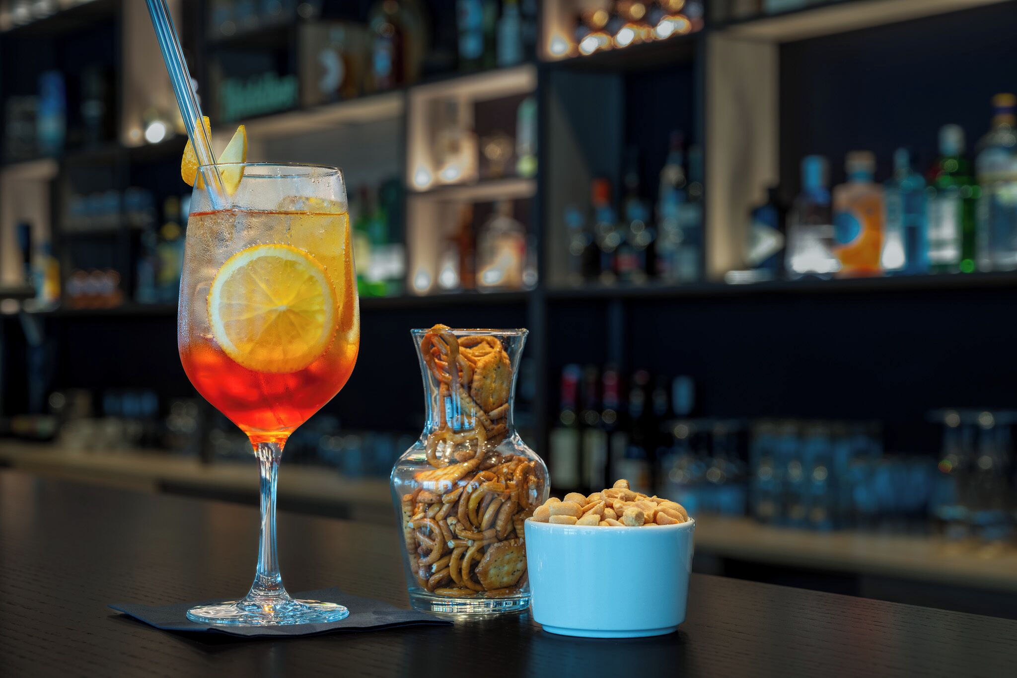 A bar setting with a cocktail glass, a jar of snacks, and a bowl of nuts.