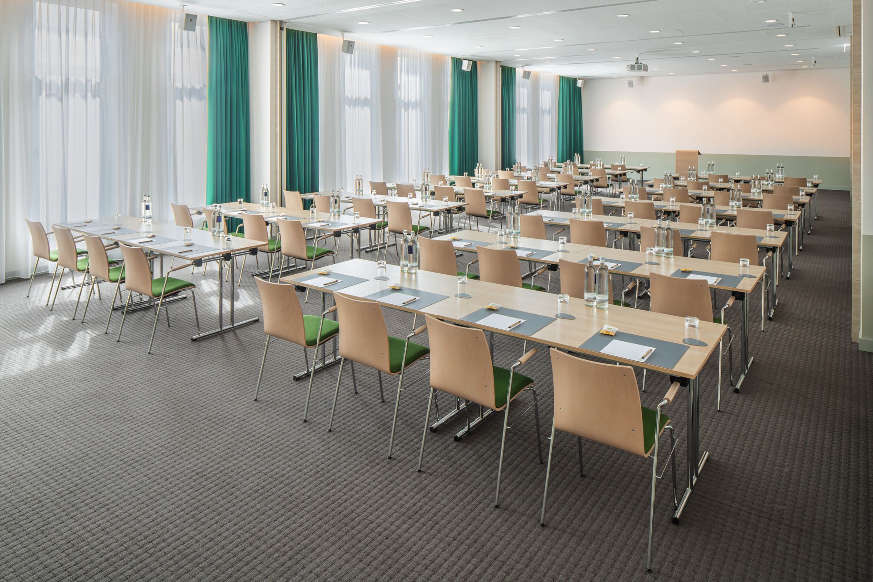 A conference room with rows of tables and chairs, equipped with water bottles and notepads.