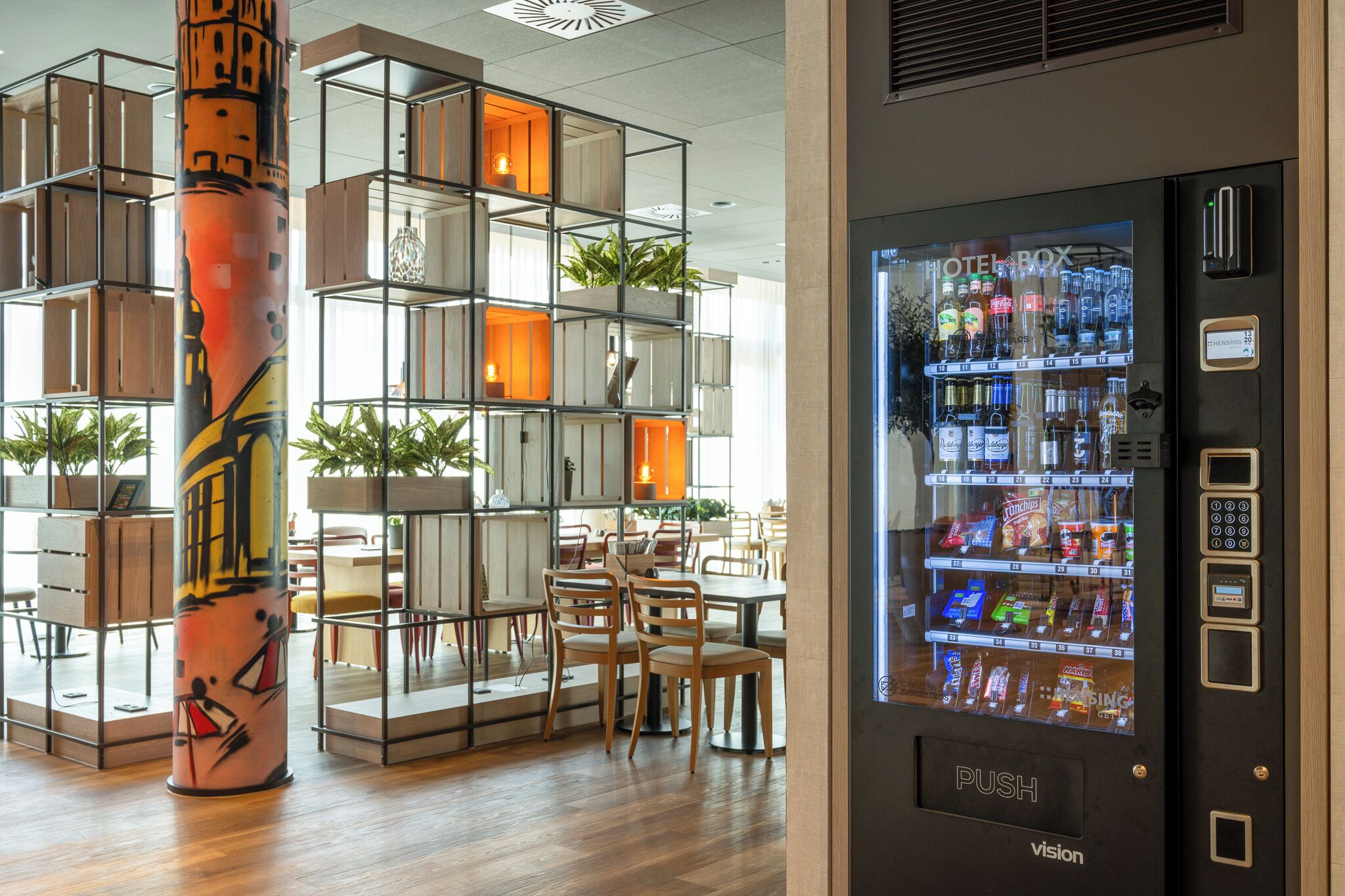 A modern hotel lobby with a vending machine, wooden furniture, and a decorative pillar.