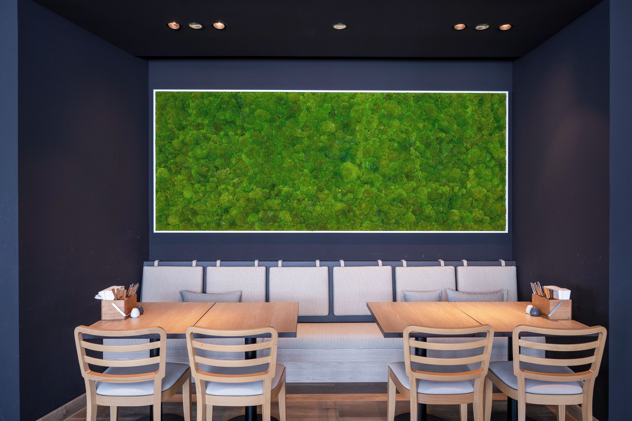 A modern dining area with a large green wall mural, cushioned seating, and wooden tables and chairs.