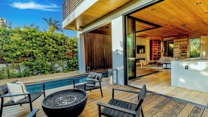 A modern outdoor deck with a pool, seating, and a fire pit.