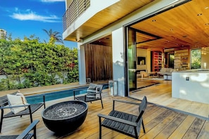 A modern outdoor deck with a pool, seating, and a fire pit.