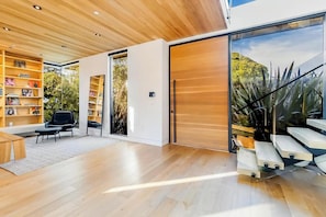 A modern interior with a wooden ceiling, built-in bookshelves, a black chair, and a staircase leading outside.
