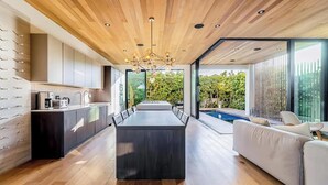 A modern kitchen with a central island, a dining area with a long table, and a pool area visible through large windows.