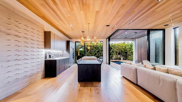 A modern interior with a wooden ceiling, a central dining area, and a seating area with a view of the outdoors.