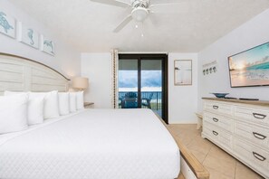 Een hotelkamer met een groot bed, een kaptafel, een plafondventilator en uitzicht op de omgeving.