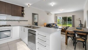 A modern kitchen with white cabinets, a built-in oven, and a dishwasher. There is a dining area with a wooden table and chairs. - 13A Elliot Avenue, Hayborough – Sea Views, Walk to Beach, Wi-Fi & Bikeway (Hayborough)