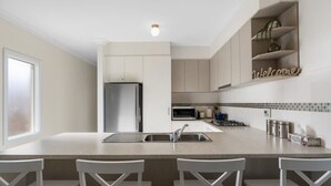 A modern kitchen with a central island, stainless steel appliances, and white cabinetry. - 13A Elliot Avenue, Hayborough – Sea Views, Walk to Beach, Wi-Fi & Bikeway (Hayborough)