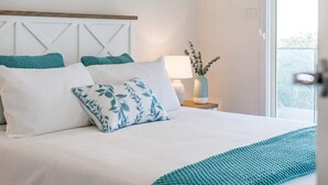 A neatly made bed with white and teal bedding, a bedside lamp, and a view of the outdoors. - 13A Elliot Avenue, Hayborough – Sea Views, Walk to Beach, Wi-Fi & Bikeway (Hayborough)