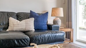 A black leather sofa with two pillows, a lamp, and a wooden side table. - 13A Elliot Avenue, Hayborough – Sea Views, Walk to Beach, Wi-Fi & Bikeway (Hayborough)