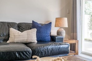 A black leather sofa with two pillows, a lamp, and a wooden side table.