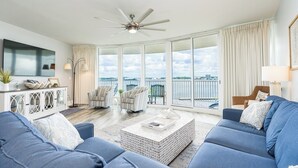 A spacious living room with a large TV, two armchairs, a sofa, and a balcony with a view of the water. - Caribe Resort | Lazy River | Indoor & Outdoor Pools | Hot Tubs | Sleeps 14 (Orange Beach)
