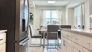 Una cocina moderna con refrigerador empotrado, un comedor con mesa y sillas, y una ventana con cortinas.