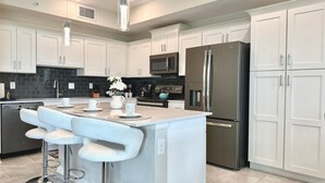 Una cocina moderna con gabinetes blancos, electrodomésticos de acero inoxidable y una isla central con taburetes de bar.