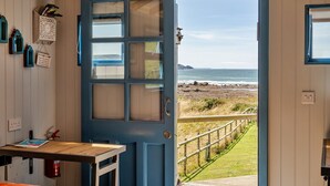 A room with a large blue door leading to a beach view. - Driftwood (Widemouth Bay)
