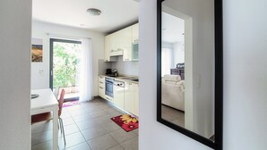 Una cocina moderna con armarios blancos, un comedor con mesa y sillas, y un espejo grande que refleja la habitación.