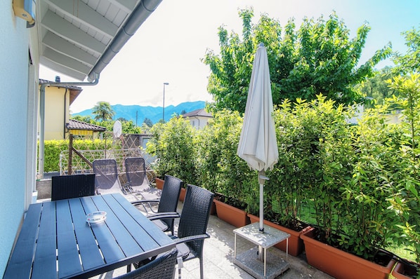 An outdoor patio with a table and chairs, surrounded by potted plants and a large umbrella. - Casa Mummi (Losone)