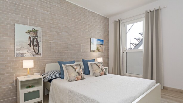 Une chambre avec un mur en briques, un lit avec une literie blanche, deux tables de chevet avec des lampes et une fenêtre avec des rideaux.