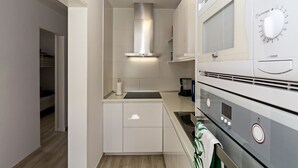 Une cuisine compacte avec des meubles blancs, une hotte de cuisinière en acier inoxydable, un four à micro-ondes et un four traditionnel.