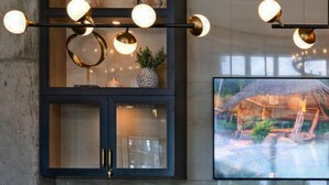 Een modern interieur met een donkere kast, een televisie die een buitenscène toont en zwarte stoelen ervoor.