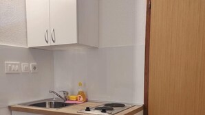 Une cuisine de taille réduite, avec des meubles blancs, un évier et une petite cuisinière.