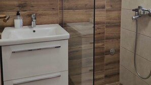 Une salle de bain moderne avec une douche à parois de verre, un lavabo blanc doté d’un distributeur de savon et un miroir au-dessus du lavabo.