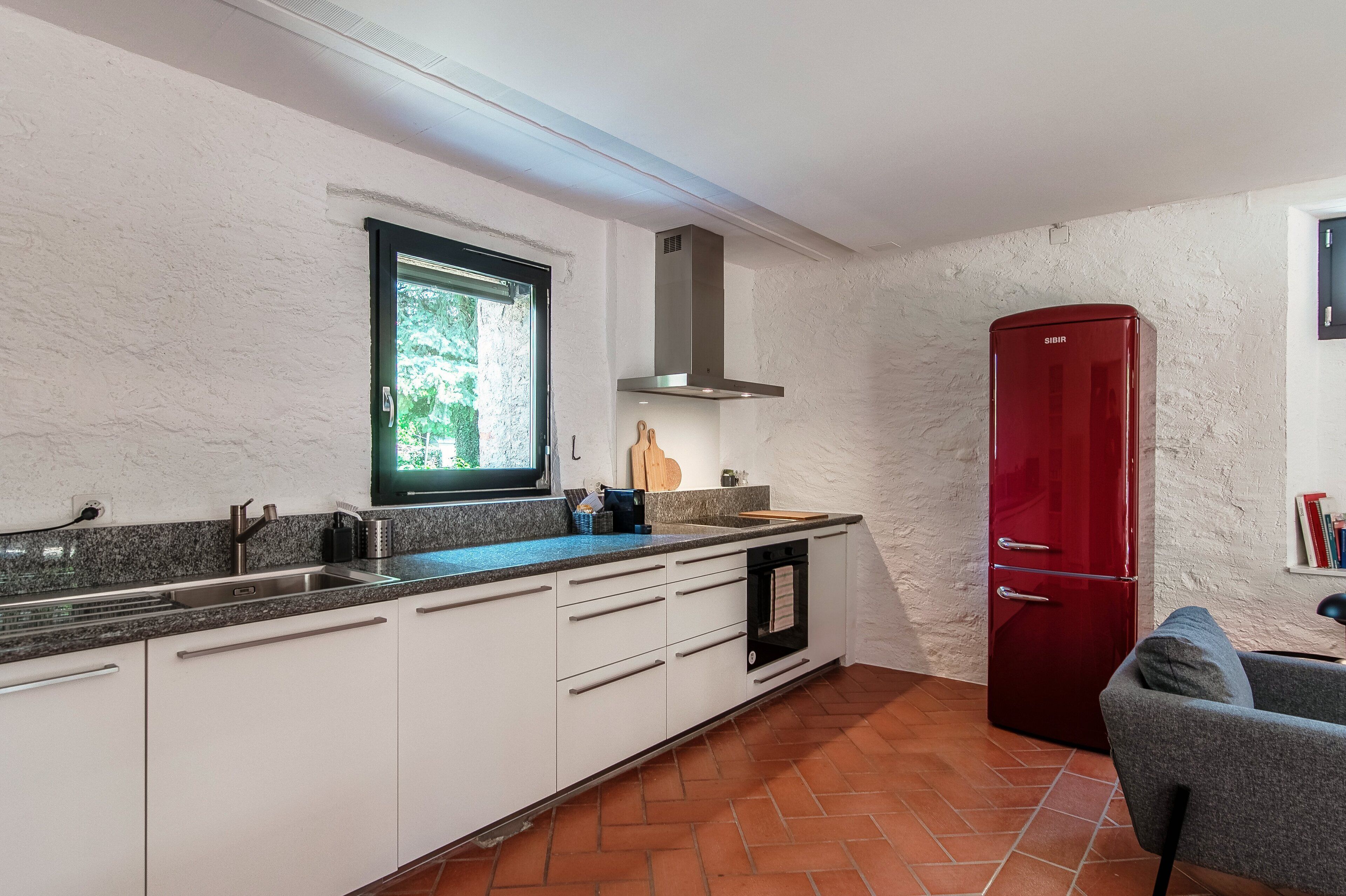 A kitchen with white cabinets, a red refrigerator, and a window providing natural light.