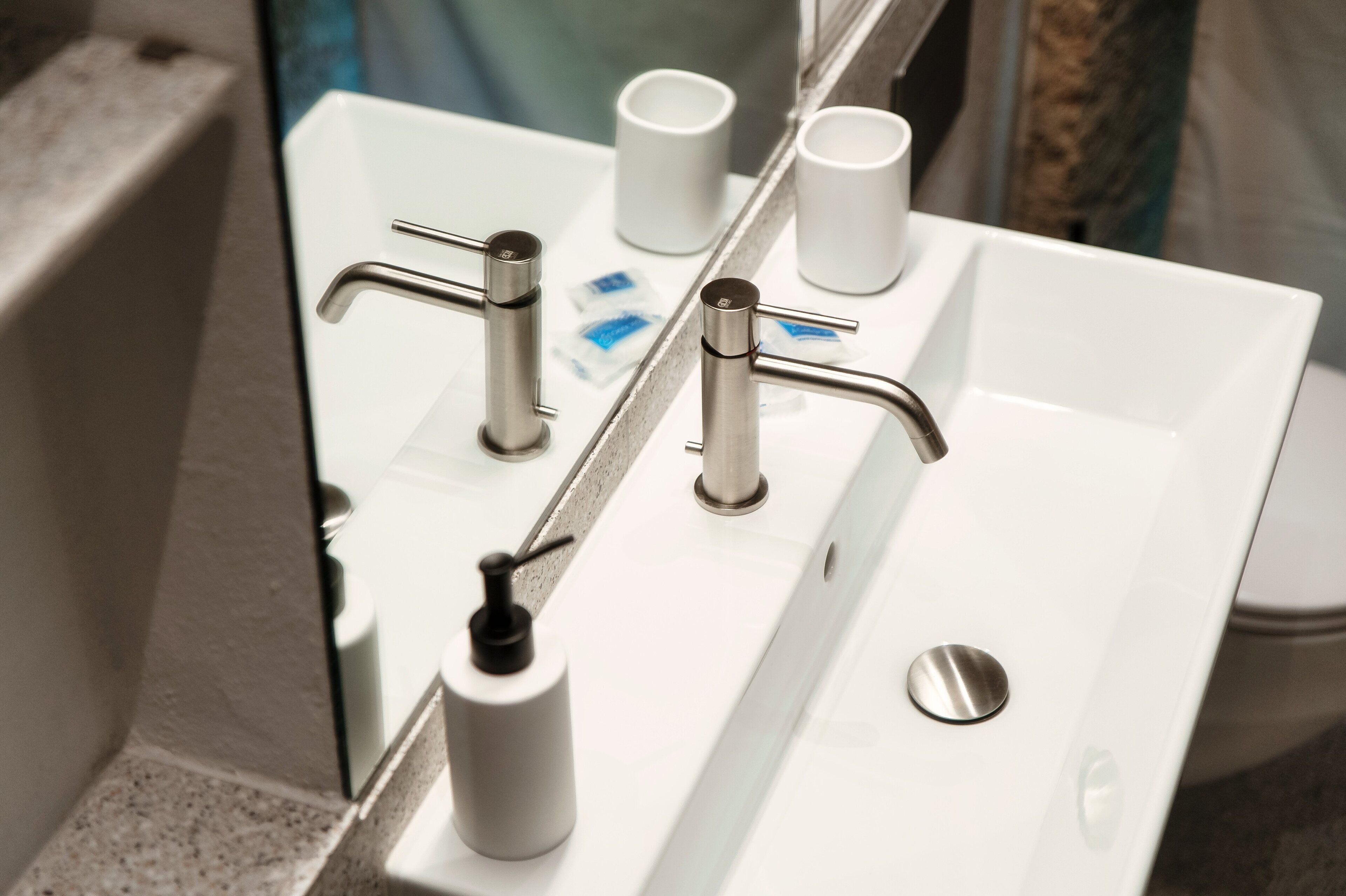 Un lavabo de bany amb un mirall, dues aigües i un dosificador de sabó.