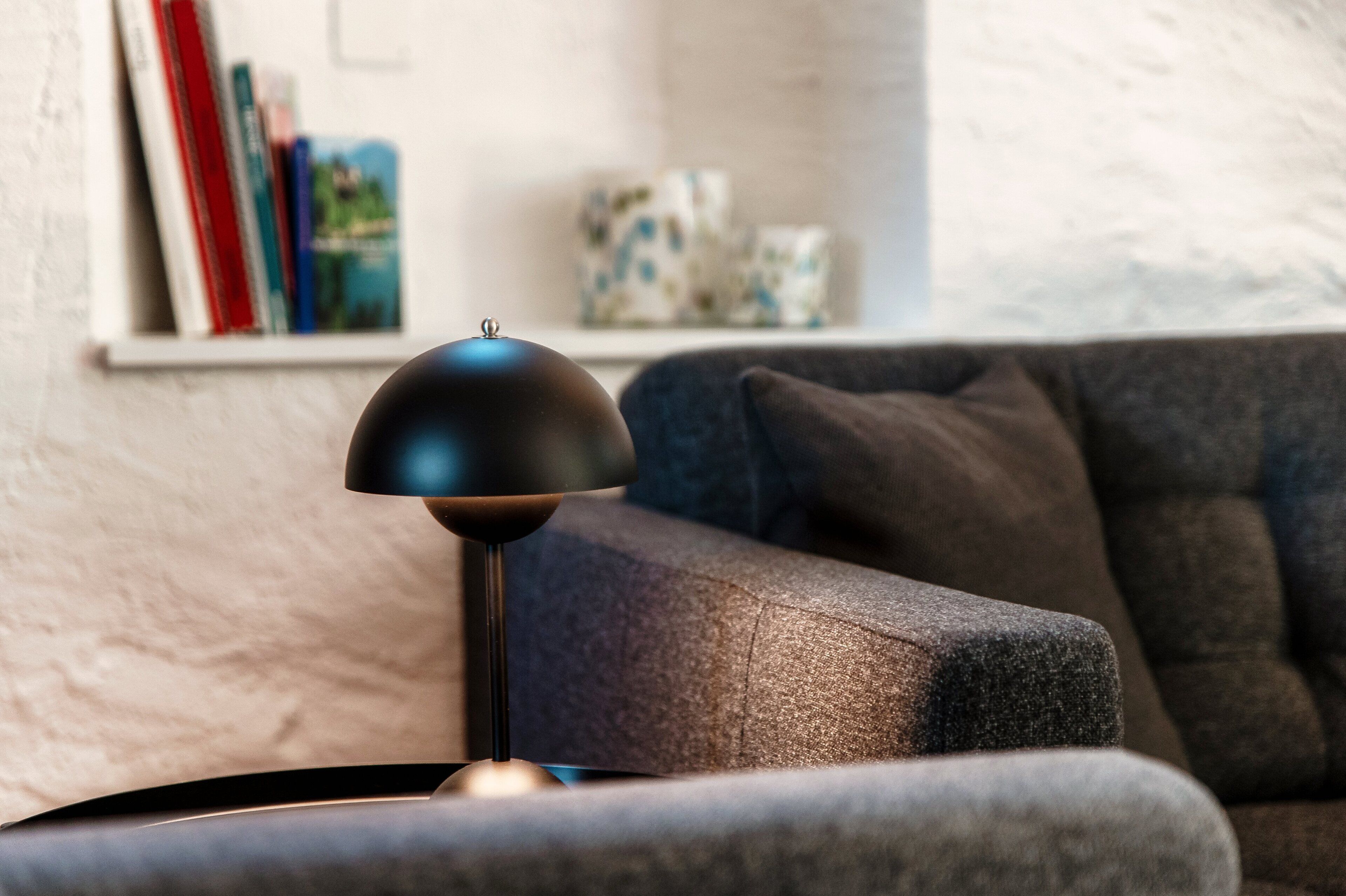 Un salon moderne avec un canapé de couleur foncée, un lampadaire noir et une bibliothèque contenant des livres et des objets décoratifs.