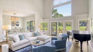 A spacious living room with a large window, a grand piano, and a white sofa. - New Listing in popular neighborhood (Kiawah Island)