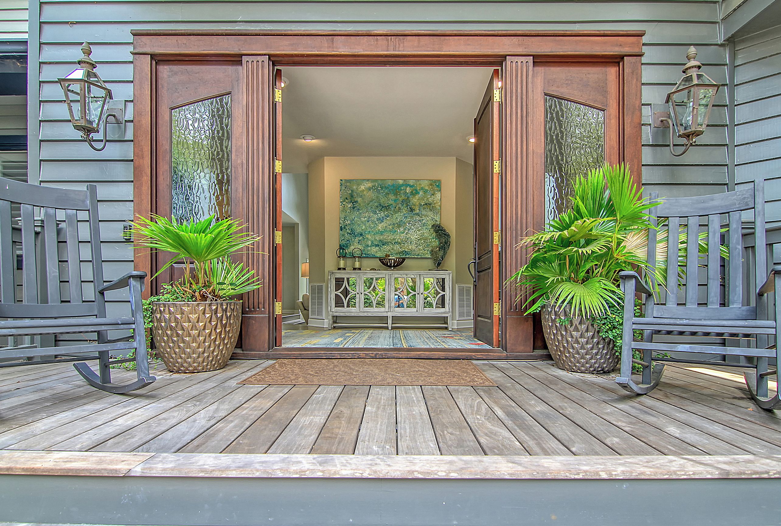A wooden deck with two rocking chairs, a potted plant, and a bench.