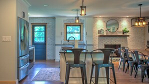 A modern kitchen with a brick wall, a fireplace, and bar stools.