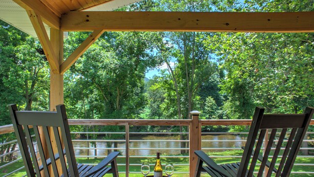 A wooden deck with two chairs and a table, a bottle, and two wine glasses.