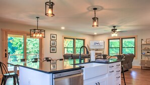 A modern kitchen with a central island, built-in appliances, and large windows offering views of greenery.